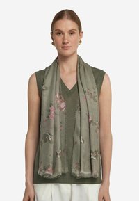 Foulard léger à motifs floraux verts avec des fleurs roses et blanches. Les bords sont frangés. Drapé sur un haut sans manches vert.