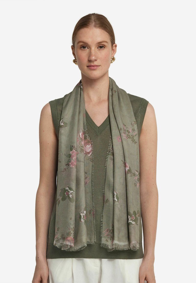 Foulard léger à motifs floraux verts avec des fleurs roses et blanches. Les bords sont frangés. Drapé sur un haut sans manches vert.