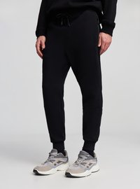 Pantaloni jogger neri realizzati in tessuto morbido con vita elastica e tasche laterali, caratterizzati da un design con gamba affusolata e polsini a costine.