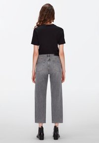 Top negro de manga corta combinado con jeans grises de pierna recta y cintura alta. Textura suave; los jeans cuentan con dos bolsillos traseros y dobladillos deshilachados.