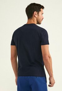 Camiseta de manga corta azul marino, fabricada en algodón, con cuello redondo, diseño ajustado, detalles mínimos, textura suave, combinada con pantalones azules.
