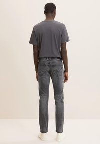 Camiseta gris combinada con jeans gris oscuro, con un corte slim, diseño de cinco bolsillos y una textura ligeramente desgastada. Zapatillas blancas completan el look.