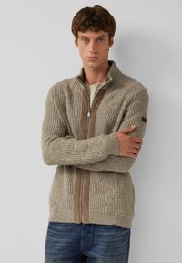 Beige rits cardigan gemaakt van gestructureerde brei stof, met een bruine suède strook in het midden en geribbelde boorden.