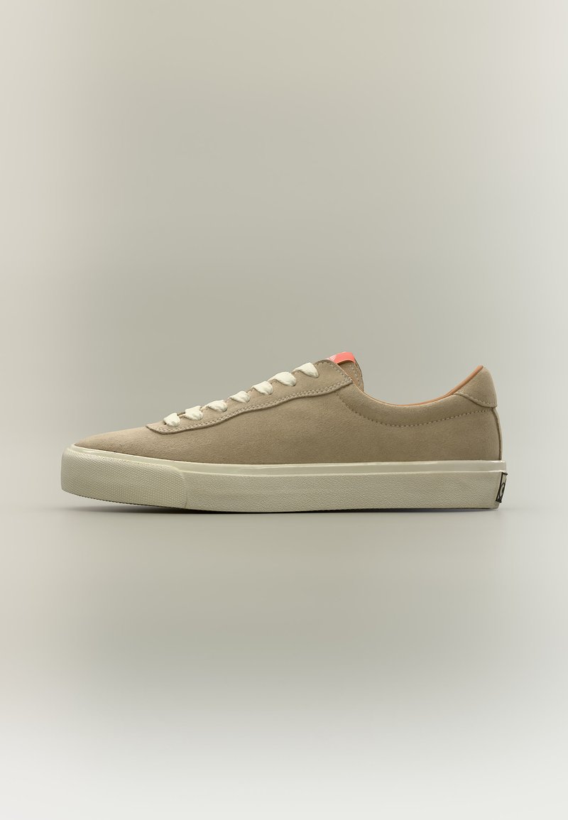 Baskets basses en daim beige avec lacets blancs et semelle épaisse en caoutchouc blanc sur fond neutre.