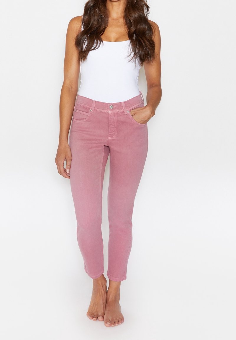 Růžové slim-fit džíny s páskem uprostřed, pěti kapsami a zapínáním na knoflík. Materiál má hladkou strukturu a mírně vybledlý vzhled.