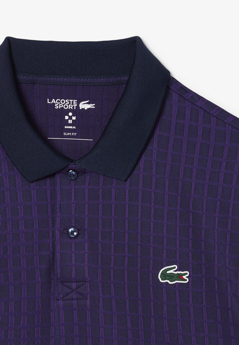 Polo shirt viola con un motivo a righe, colletto blu navy, tre bottoni e logo Lacoste sul petto sinistro. Design slim fit e tessuto strutturato.