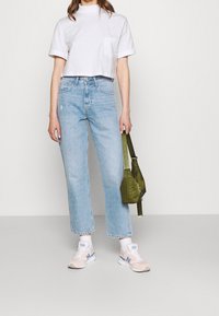 Bílé cropped tričko, světle modré rovné džíny, růžovo-modré tenisky a zelená taška přes rameno. Jednoduchý design, ležérní styl.