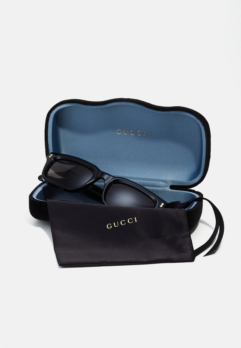 Occhiali da sole neri Gucci all'interno di un'astuccio morbido foderato di blu. Include un panno per la pulizia nero con scritte dorate. Design elegante con lenti scure.