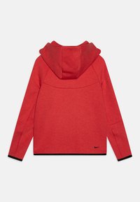 Felpa rossa con cappuccio in tessuto testurizzato, dotata di cappuccio e rifiniture nere ai polsini e alla base. Logo Nike nero posizionato in basso a destra.