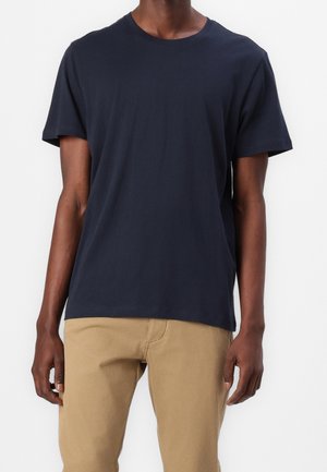 Marineblaues Baumwoll-T-Shirt, kurze Ärmel, Rundhalsausschnitt, lockere Passform, kombiniert mit beigen Chinos. Glatte Textur, schlichtes Design, keine sichtbaren Muster.