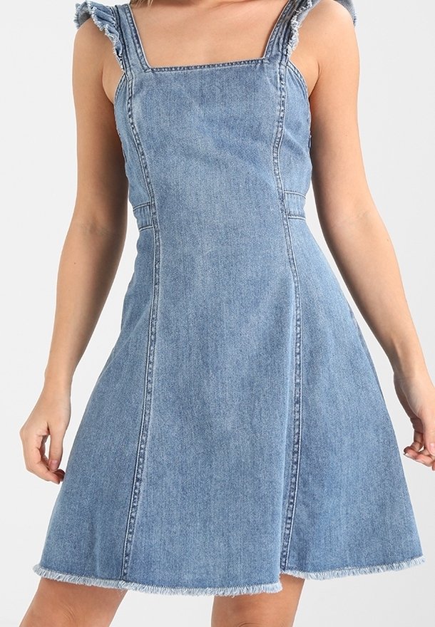 Denimmekko, jossa on neliön muotoinen kaula-aukko, rypytetyt hihnat ja liehuva hame. Vaalea sininen väri, jossa on revitty helma ja selkeät saumat.
