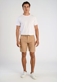 Beige texturerade shorts med elastisk midja och dragsko, ihop med en enkel vit t-shirt och vita sneakers.