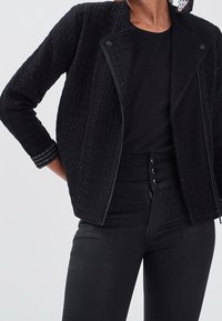 Czarna pikowana kurtka o teksturowanej powierzchni, z zamkiem błyskawicznym, stojącym kołnierzem oraz metalicznymi akcentami na mankietach.