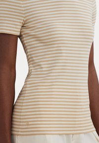 Striped t-shirt in beige and light cream, fitted design, short sleeves, soft texture, featuring a subtle logo on the hem.