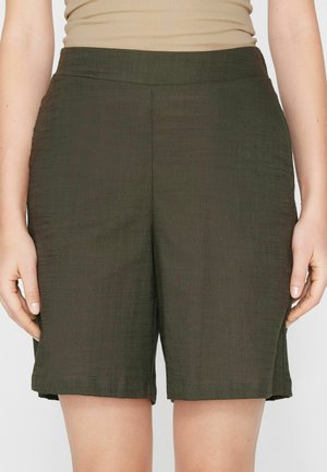 Vista desde la cintura hasta la mitad del muslo de una persona que lleva pantalones cortos sueltos de textura verde oscuro y una camiseta sin mangas beige con relieve.