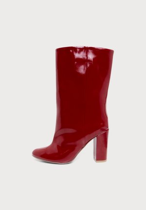 Botte rouge brillante montant jusqu’au genou, à bout arrondi et à haut talon bloc.