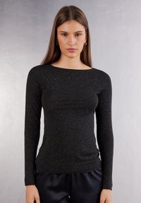 Sort langærmet top lavet af et struktureret, spottet stof; har en bådudskæring og en tætsiddende silhuet. Passer til mørke satinbukser.