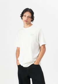 White cotton t-shirt with a crew neck and short sleeves. Features a small light green Adidas logo on the left chest.