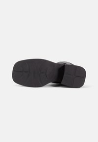 Semelle de chaussure noire avec une finition lisse. Présente un motif strié pour une meilleure adhérence et un design durable et flexible. Talon plat sans accents proéminents.