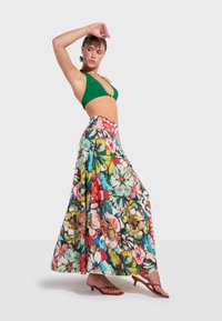 Groene bikini-top gecombineerd met een lange, met bloemen patgeijke rok in levendige kleuren. De rok heeft een vloeiende snit en een tailleband.