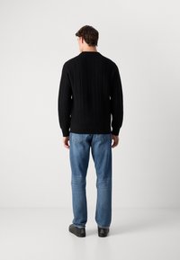 Black knitted sweater with ribbed texture, round neckline, and long sleeves, paired with light blue jeans and black shoes.