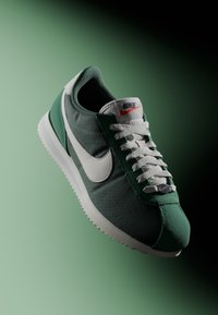 Green and grey athletic shoe with fabric upper, white swoosh logo, grey laces, and textured sole. Features classic design and clean lines.