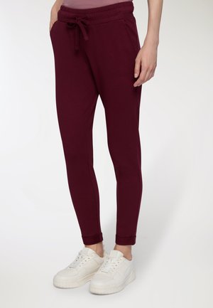 Pantaloni jogger bordeaux con vita elasticizzata e cordoncino, dotati di tasche laterali e caviglie affusolate, abbinati a sneaker bianche.