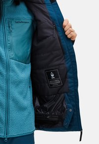 Blue and teal jacket with fleece exterior, quilted lining, and zippered pockets. Contains care label and closure details inside.