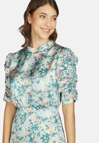 Blumen-satin-kleid in grün, mit einem hohen Ausschnitt, puffärmel mit elastischen Rüschen und einer taillierten Taille. Zarte Blattmuster durchgehend.