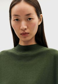 Sweatshirt vert avec un col haut à côtes. Le tissu semble doux avec une texture lisse, sans coutures ni motifs visibles.
