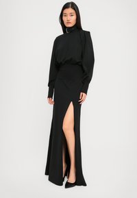 Schwarzes, langärmliges Kleid mit hohem Kragen, seitlichem Schlitz und taillierter Passform, aus glattem Stoff, mit Puffärmeln und strukturiertem Kragen.