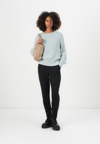 Svetlo modra pletena jopica z dolgimi rokavi, črne tesne hlače in črne platform čevlje; drži bež tkaninsko torbo.