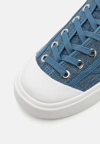 Blå denim sneakers med hvit gummikappe og såle, med runde metallhull og teksturerte lisser.