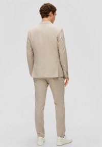 Beige geruite pak met op maat gemaakte blazer en taps toelopende broek, gemaakt van een textuurstof. Gecombineerd met witte sneakers voor een casual uitstraling.