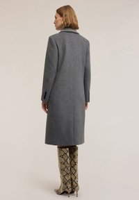 Cappotto grigio in lana con vestibilità su misura, maniche lunghe e colletto a punte. Abbinato a stivali al ginocchio con motivo in pelle di serpente.