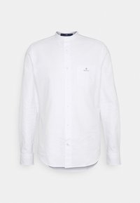 Valkoinen pitkähiha shirt, jossa on bändikaulus, napitettava etuosa ja rintatasku, jossa on sininen logo. Valmistettu kevyestä kankaasta.