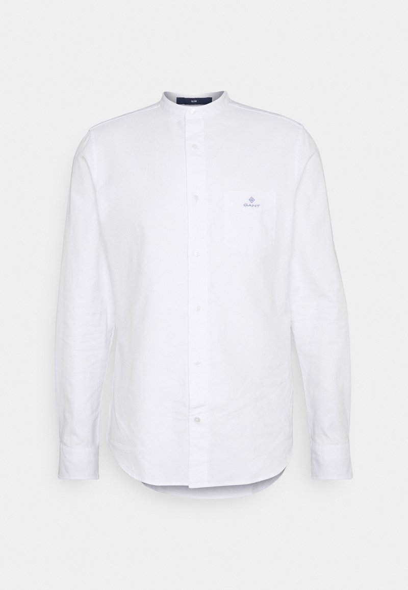 Valkoinen pitkähiha shirt, jossa on bändikaulus, napitettava etuosa ja rintatasku, jossa on sininen logo. Valmistettu kevyestä kankaasta.