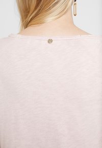 Helles Rosa, weicher Stoffoberteil mit einem rohen Ausschnitt und einem kleinen metallischen Akzent auf der Rückseite. Einfacher, lockerer Schnitt, keine sichtbaren Muster.