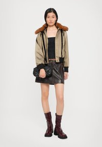 Tan bomber jacket with brown fur trim, black cropped top, brown leather mini skirt, and glossy burgundy ankle boots. Black quilted handbag.
