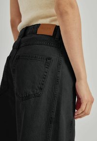 Svarta denimbyxor med hög midja, med en läderlapp märkt "NORR" och en synlig ficka sydd på baksidan.