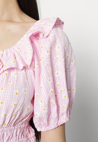Blusa listrada em rosa e branco com bordado de margaridas brancas e centros amarelos, apresentando um decote com babados e mangas bufantes.