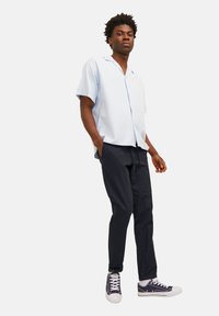 Chemise bleu clair à manches courtes avec col ouvert ; associée à un pantalon sombre et des baskets bleu marine. Texture lisse, coupe décontractée, design simple.
