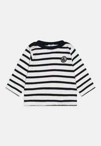 Camisa de manga longa com riscas em branco e azul-marinho, apresentando um decote redondo e um detalhe de botão decorativo no ombro. Pequeno logotipo no peito.
