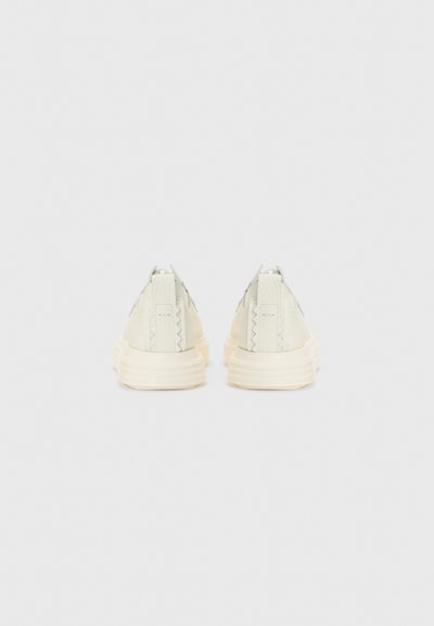 Hvide teksturerede sneakers med gummisål, der har et low-top design, flade snørebånd og subtile syninger på hælflapperne.