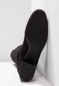 Bottine en daim noir avec un talon carré, dotée d'une semelle lisse et d'un logo subtil embossé sur le talon. Design robuste et épuré.