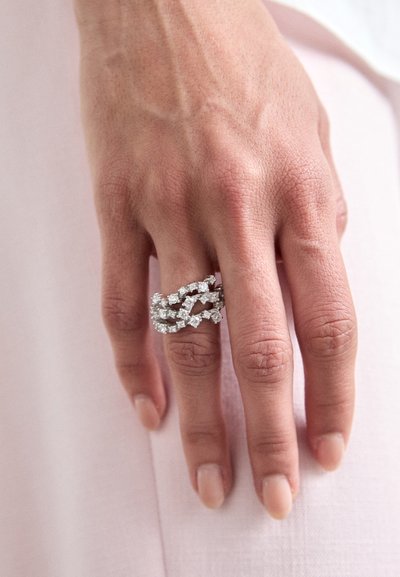 Trois anneaux en argent entrelacés avec des accents de diamant étincelants. Texture lisse, finition polie et détails complexes dans le design.