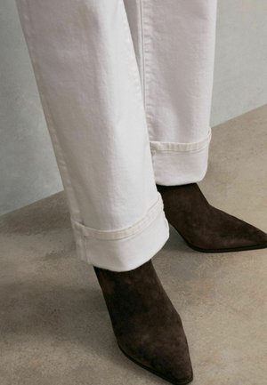 White denim jeans with rolled cuffs paired with dark brown suede pointed-toe heels. The texture of the fabric is smooth and the heel is sleek.