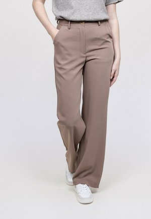 Personne portant un pantalon large taupe avec poches et des baskets blanches, associé à un haut en maille gris à manches courtes.