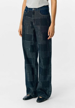 Weite Denim-Hosen mit einem strukturierten Patchwork-Design in Dunkelblau mit gestreiften und gepunkteten Mustern. Enthält Fronttaschen und einen Taillenbund.