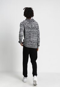 Grau-schwarzer Kapuzenpullover mit Kängurutasche, strukturierter Stoff und Kapuze mit Kordelzug, kombiniert mit schwarzen Hosen und weißen Turnschuhen.